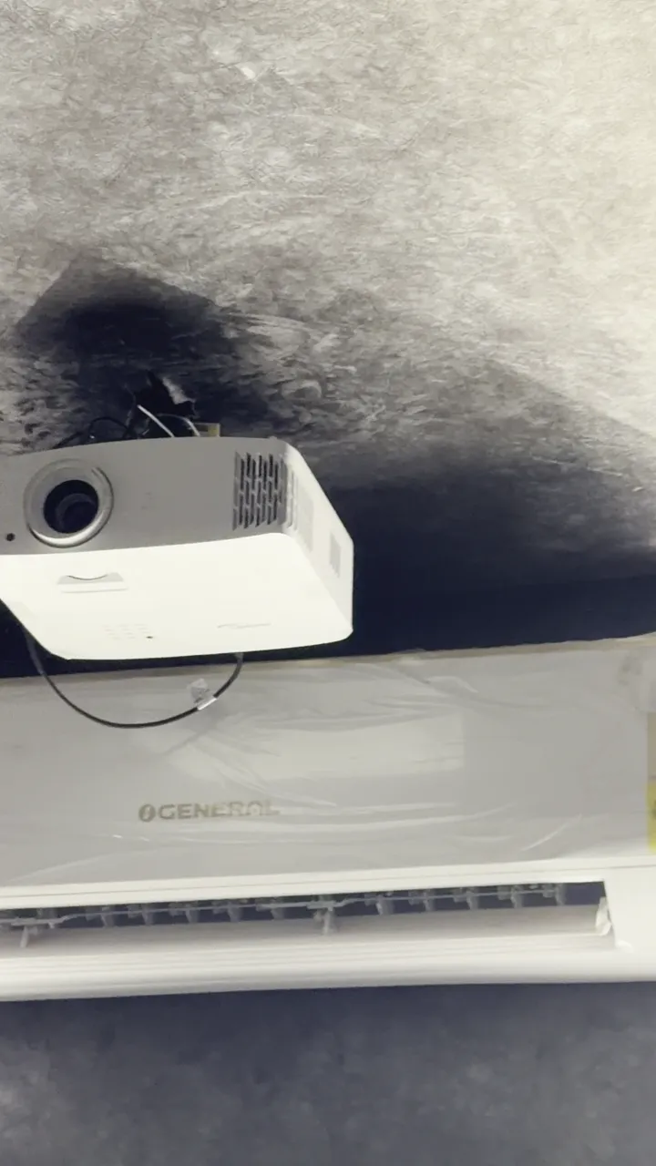 Ceiling-mounted white projector beside an air-conditioning unit in original SLV source footage